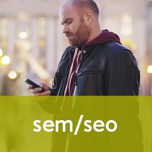 An image of a man using his phone to connect/find information online (text overlay: SEO/SEM)