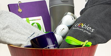A collection of branded promotional items in a bowl engraved with the words “Happy & Healthy”